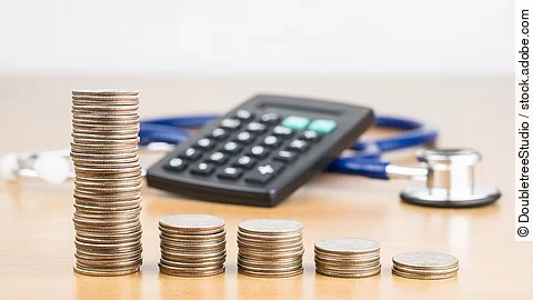 Stapel aus Münzen vor einem Taschenrechner und Stethoskop