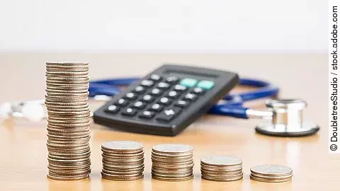 Finanzen Stapel aus Münzen vor einem Taschenrechner und Stethoskop