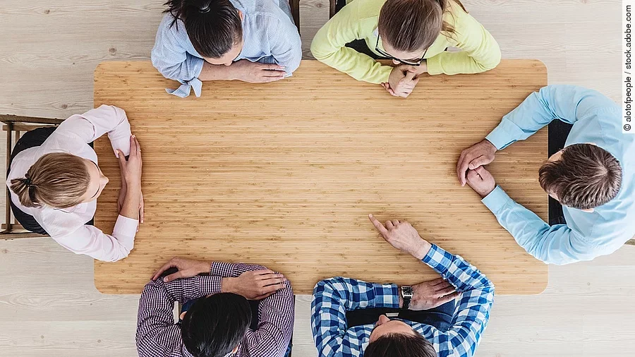 Gesprächsrunde mit sechs Personen an einem hölzernen Tisch