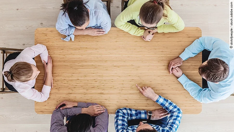 Gesprächsrunde mit sechs Personen an einem hölzernen Tisch
