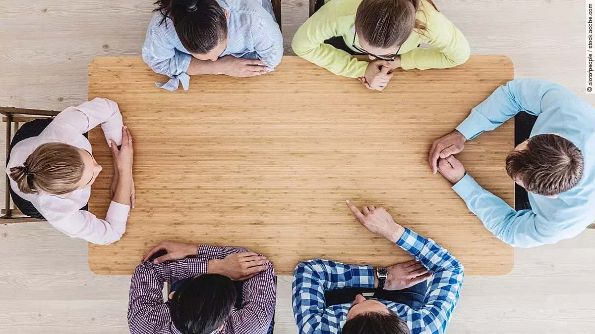 Gesprächsrunde mit sechs Personen an einem hölzernen Tisch