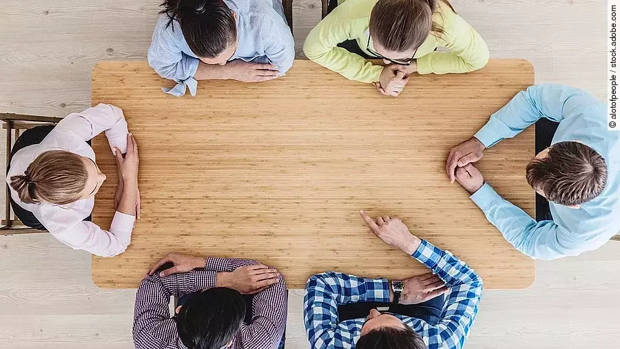 Gesprächsrunde mit sechs Personen an einem hölzernen Tisch