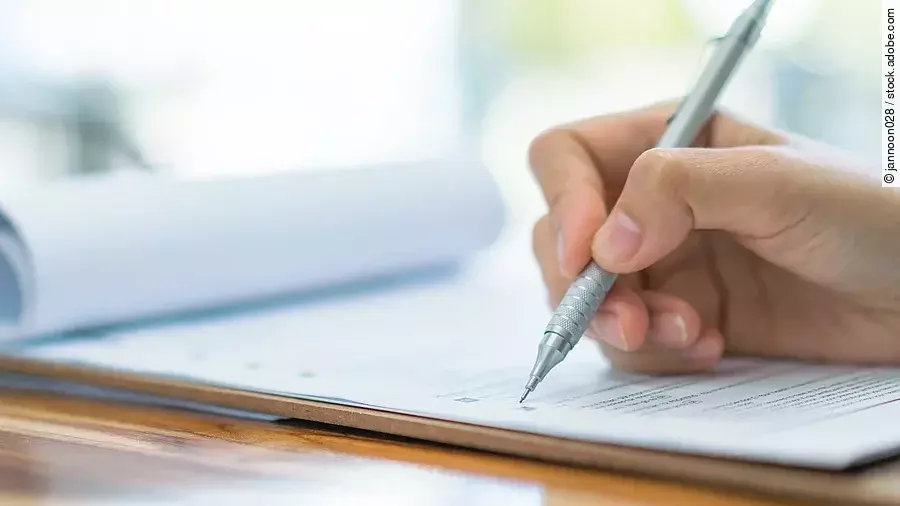 Eine Hand hält einen Stift und schreibt auf ein Prüfungsdokument.