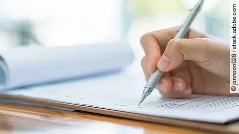 Eine Hand hält einen Stift und schreibt auf ein Prüfungsdokument.