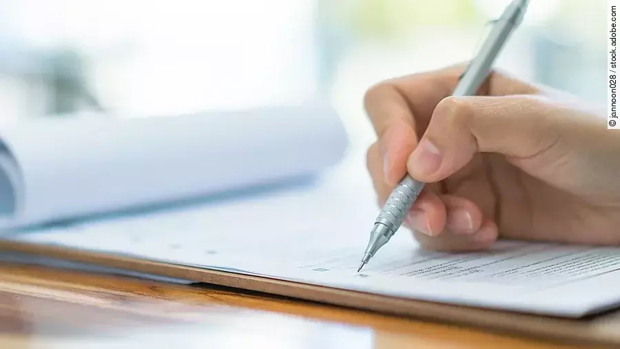 Eine Hand hält einen Stift und schreibt auf ein Prüfungsdokument.