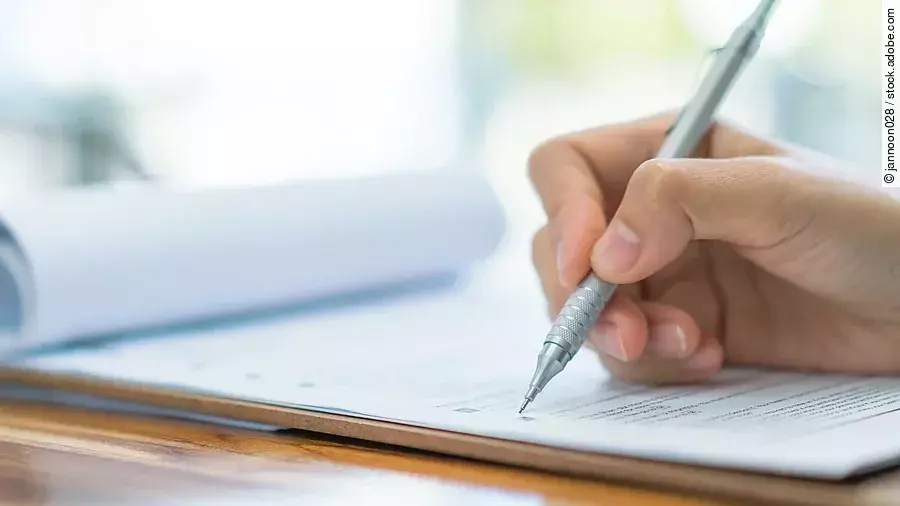 Eine Hand hält einen Stift und schreibt auf ein Prüfungsdokument.