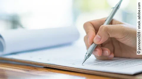 Eine Hand hält einen Stift und schreibt auf ein Prüfungsdokument.