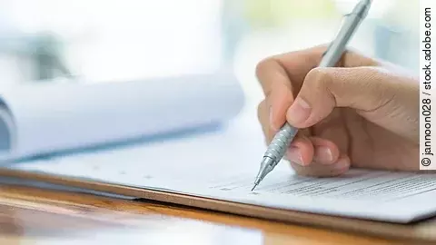 Eine Hand hält einen Stift und schreibt auf ein Prüfungsdokument.