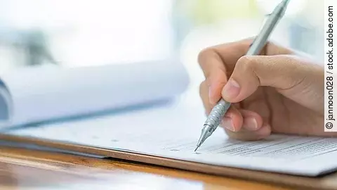 Eine Hand hält einen Stift und schreibt auf ein Prüfungsdokument.