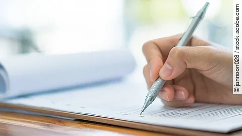 Eine Hand hält einen Stift und schreibt auf ein Prüfungsdokument.