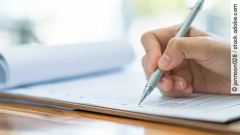 Eine Hand hält einen Stift und schreibt auf ein Prüfungsdokument.
