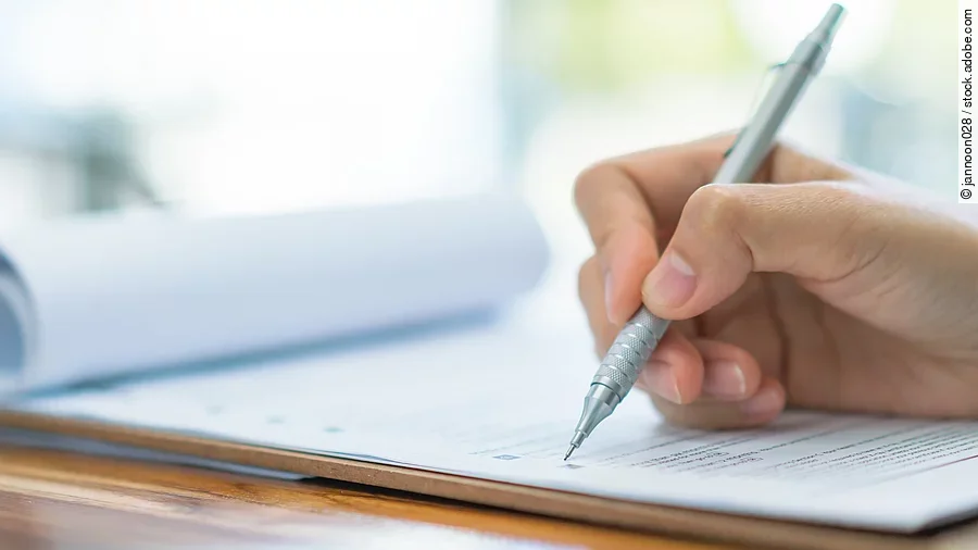 Prüfung Eine Hand hält einen Stift und schreibt auf ein Prüfungsdokument.