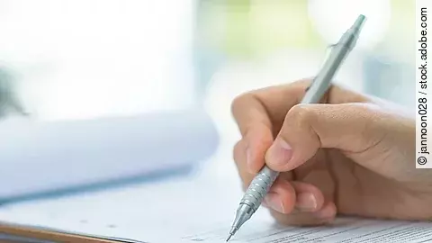 Eine Hand hält einen Stift und schreibt auf ein Prüfungsdokument.