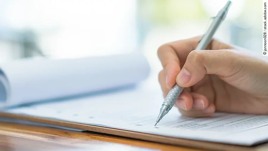 Prüfung Eine Hand hält einen Stift und schreibt auf ein Prüfungsdokument.