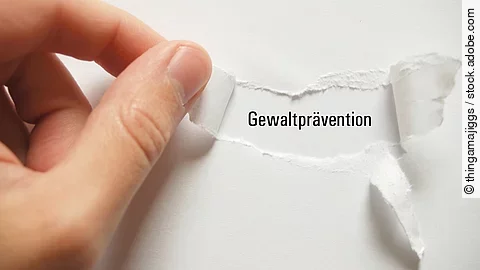 Eine Hand reißt in einem Papier den Schriftzug "Gewaltprävention" frei.