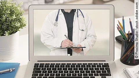 Ein aufgeklappter Laptop steht auf einem Tisch. Der Bildschirm zeigt den Torso eines Arztes.