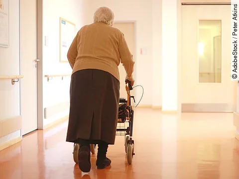 Frau mit Rollator im Gang eines Seniorenheims