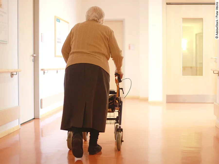 Frau mit Rollator im Gang eines Seniorenheims