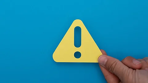 Eine Hand hält ein gelbes Dreieck mit Ausrufezeichen vor blauem Hintergrund