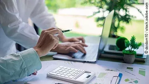 Zwei Personen in einer Besprechung. Vor ihnen ein aufgeklappter Laptop, Dokumente, Statistiken und ein Taschenrechner.