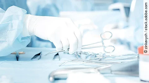 Chiurgie Hand greift nach OP-Schere, die auf einem Tisch mit weiterem OP-Besteck liegt.