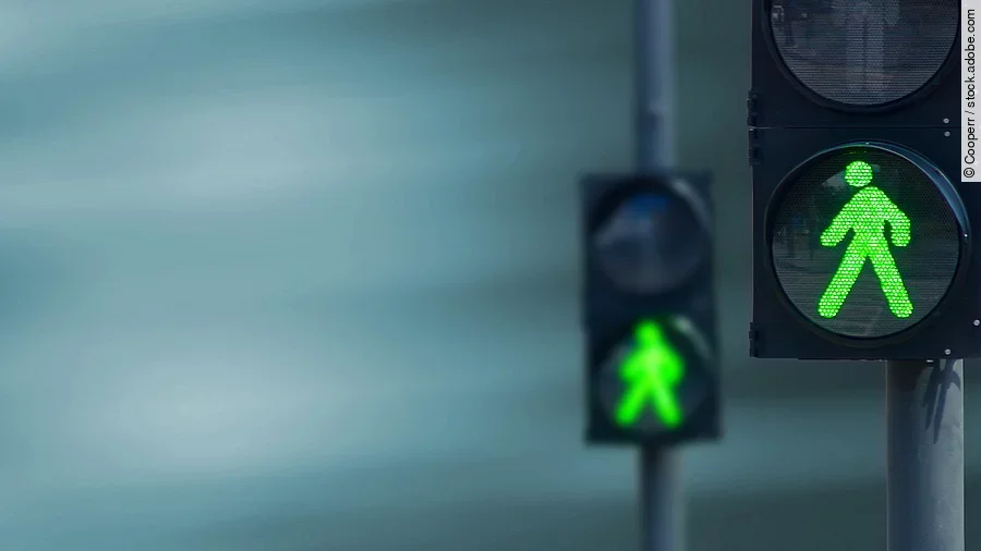 Zwei Fußgängerampeln hintereinander, die beide auf grüne Ampelmännchen geschalten sind.