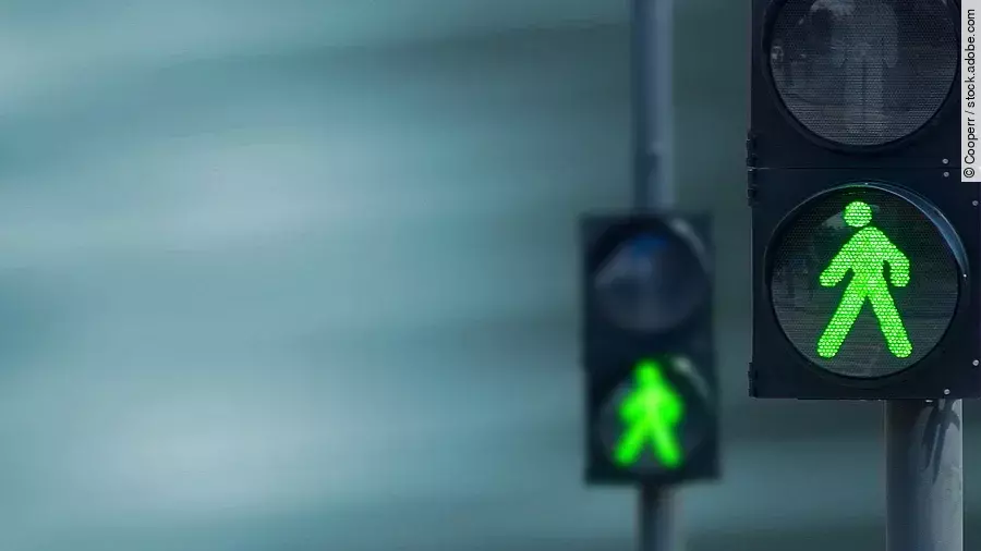Zwei Fußgängerampeln hintereinander, die beide auf grüne Ampelmännchen geschalten sind.