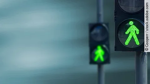Zwei Fußgängerampeln hintereinander, die beide auf grüne Ampelmännchen geschalten sind.