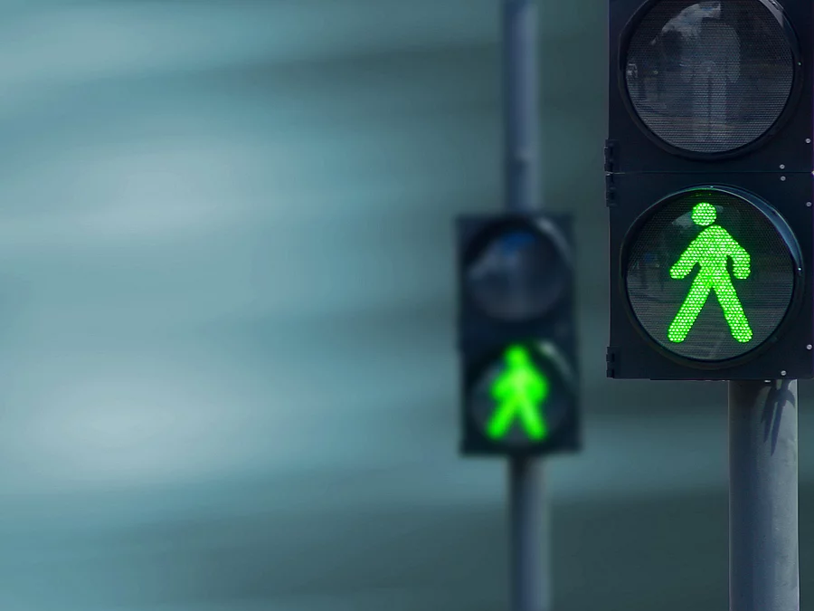 Zwei Fußgängerampeln hintereinander, die beide auf grüne Ampelmännchen geschalten sind.