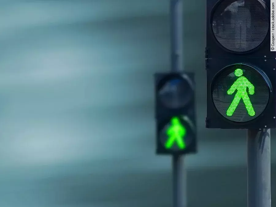 Zwei Fußgängerampeln hintereinander, die beide auf grüne Ampelmännchen geschalten sind.