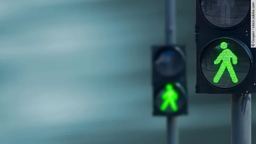 Zwei Fußgängerampeln hintereinander, die beide auf grüne Ampelmännchen geschalten sind.