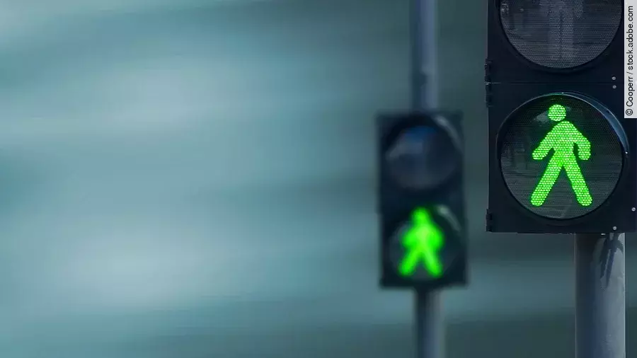 Zwei Fußgängerampeln hintereinander, die beide auf grüne Ampelmännchen geschalten sind.