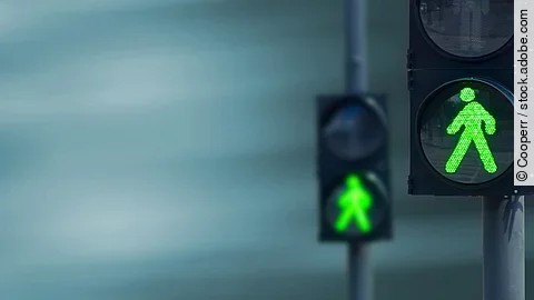 Zwei Fußgängerampeln hintereinander, die beide auf grüne Ampelmännchen geschalten sind.