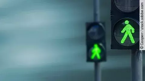 Zwei Fußgängerampeln hintereinander, die beide auf grüne Ampelmännchen geschalten sind.