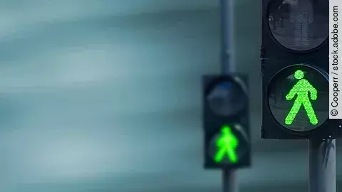 Zwei Fußgängerampeln hintereinander, die beide auf grüne Ampelmännchen geschalten sind.