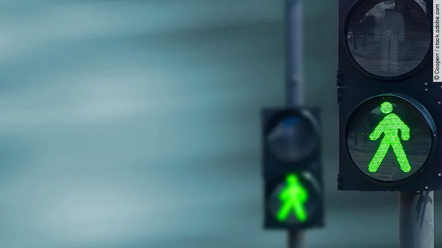 Zwei Fußgängerampeln hintereinander, die beide auf grüne Ampelmännchen geschalten sind.
