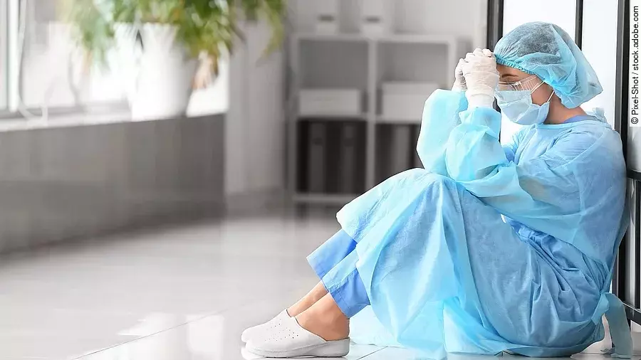 Belastetes medizinisches Personal sitzt am Boden eines Krankenhausflures.