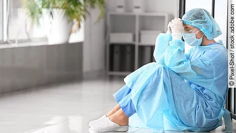 Belastetes medizinisches Personal sitzt am Boden eines Krankenhausflures.