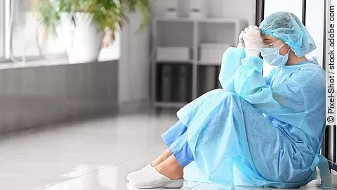 Belastetes medizinisches Personal sitzt am Boden eines Krankenhausflures.