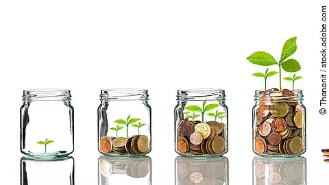 Investition Fünf Gläser stehen nebeneinander. Das linke ist leer, das rechte gänzlich mit Münzen gefüllt. Dazwischen steigt die Menge der Münzen. Aus den Münzen wächst eine Pflanze, die mit zunehmender Geldsumme immer größer wird.
