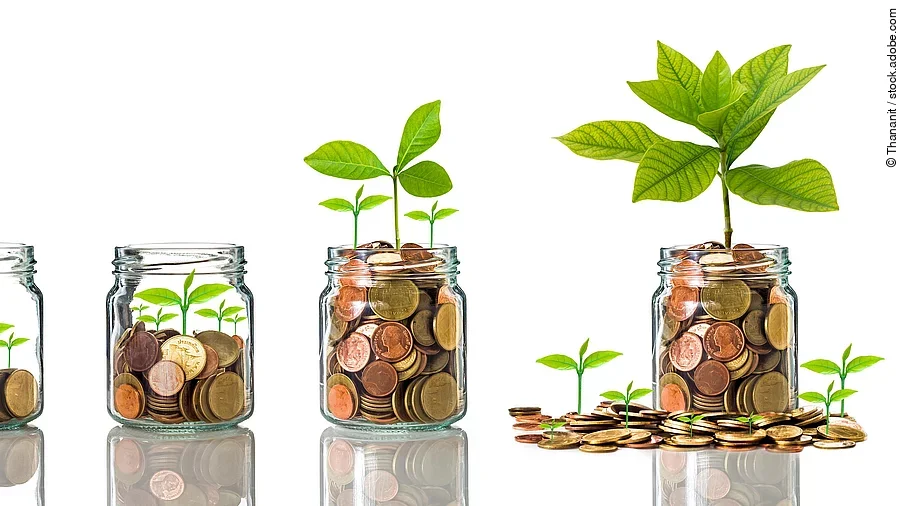 Investition Fünf Gläser stehen nebeneinander. Das linke ist leer, das rechte gänzlich mit Münzen gefüllt. Dazwischen steigt die Menge der Münzen. Aus den Münzen wächst eine Pflanze, die mit zunehmender Geldsumme immer größer wird.