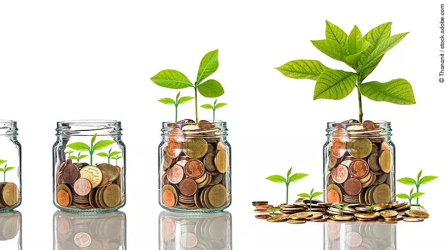 Fünf Gläser stehen nebeneinander. Das linke ist leer, das rechte gänzlich mit Münzen gefüllt. Dazwischen steigt die Menge der Münzen. Aus den Münzen wächst eine Pflanze, die mit zunehmender Geldsumme immer größer wird.