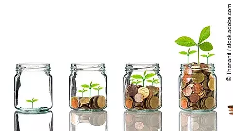 Fünf Gläser stehen nebeneinander. Das linke ist leer, das rechte gänzlich mit Münzen gefüllt. Dazwischen steigt die Menge der Münzen. Aus den Münzen wächst eine Pflanze, die mit zunehmender Geldsumme immer größer wird.