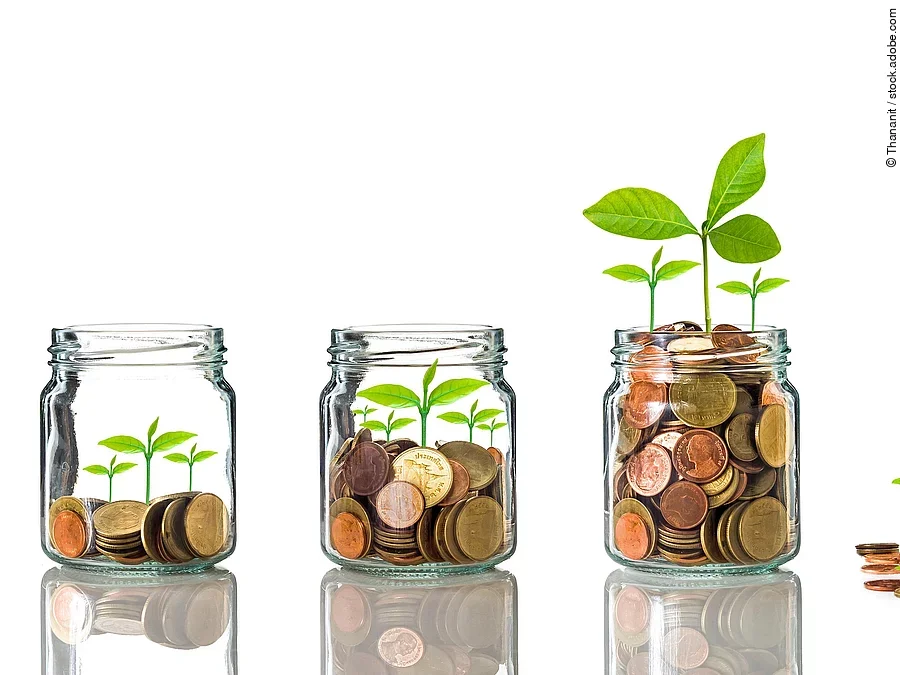 Investition Fünf Gläser stehen nebeneinander. Das linke ist leer, das rechte gänzlich mit Münzen gefüllt. Dazwischen steigt die Menge der Münzen. Aus den Münzen wächst eine Pflanze, die mit zunehmender Geldsumme immer größer wird.