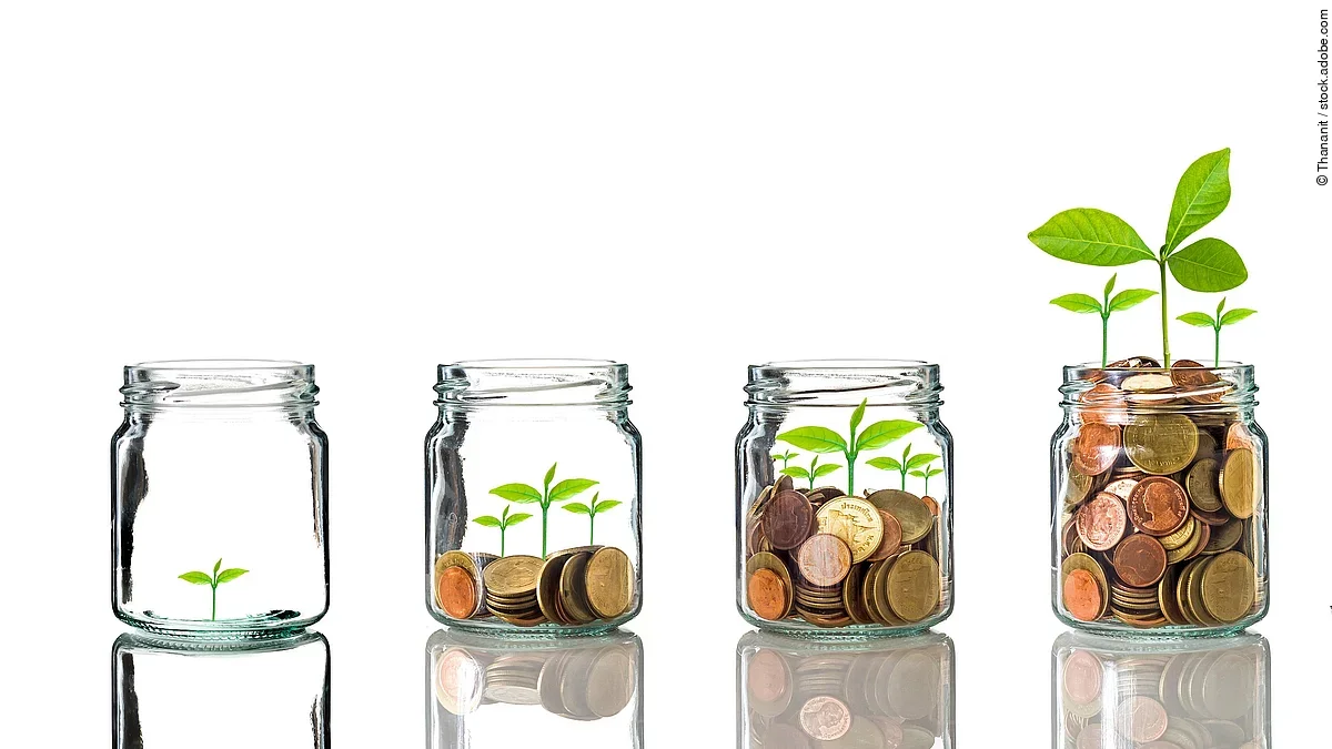 Fünf Gläser stehen nebeneinander. Das linke ist leer, das rechte gänzlich mit Münzen gefüllt. Dazwischen steigt die Menge der Münzen. Aus den Münzen wächst eine Pflanze, die mit zunehmender Geldsumme immer größer wird.