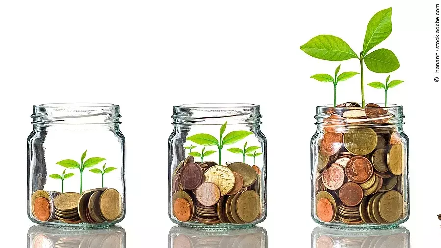 Fünf Gläser stehen nebeneinander. Das linke ist leer, das rechte gänzlich mit Münzen gefüllt. Dazwischen steigt die Menge der Münzen. Aus den Münzen wächst eine Pflanze, die mit zunehmender Geldsumme immer größer wird.