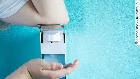 Eine Person betätigt einen Desinfektionsspender mit dem Ellenbogen.