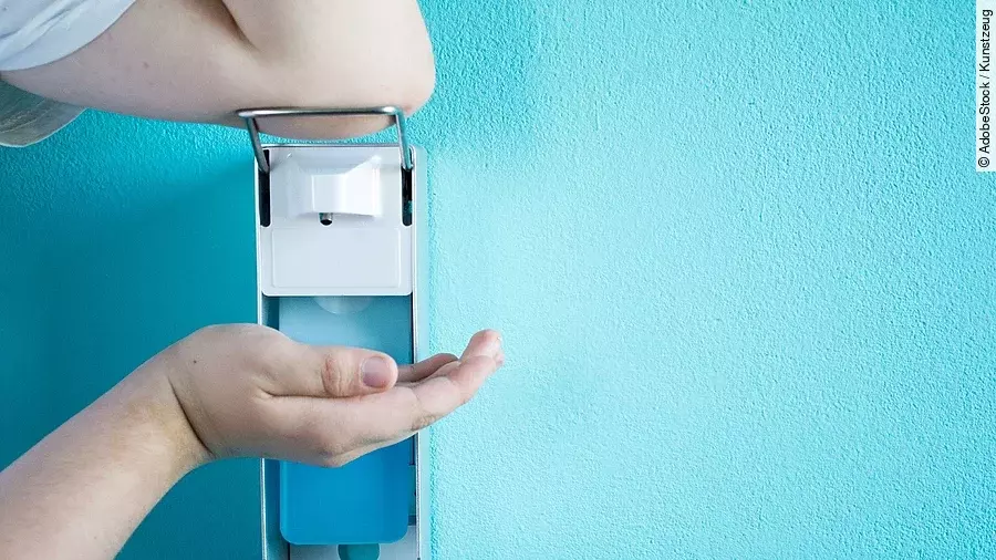 Eine Person betätigt einen Desinfektionsspender mit dem Ellenbogen.