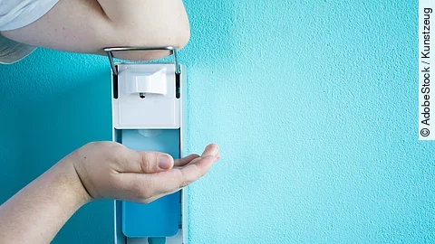 Eine Person betätigt einen Desinfektionsspender mit dem Ellenbogen.