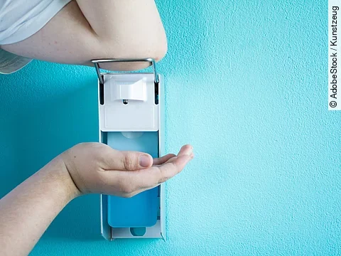 Eine Person betätigt einen Desinfektionsspender mit dem Ellenbogen.